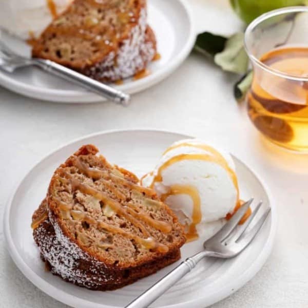 Slice of easy apple bundt cake and a scoop of ice cream on a white plate, both drizzled with caramel sauce.