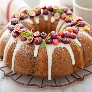 Cranberry bundt cake topped with glaze and fresh cranberries on a wire rack