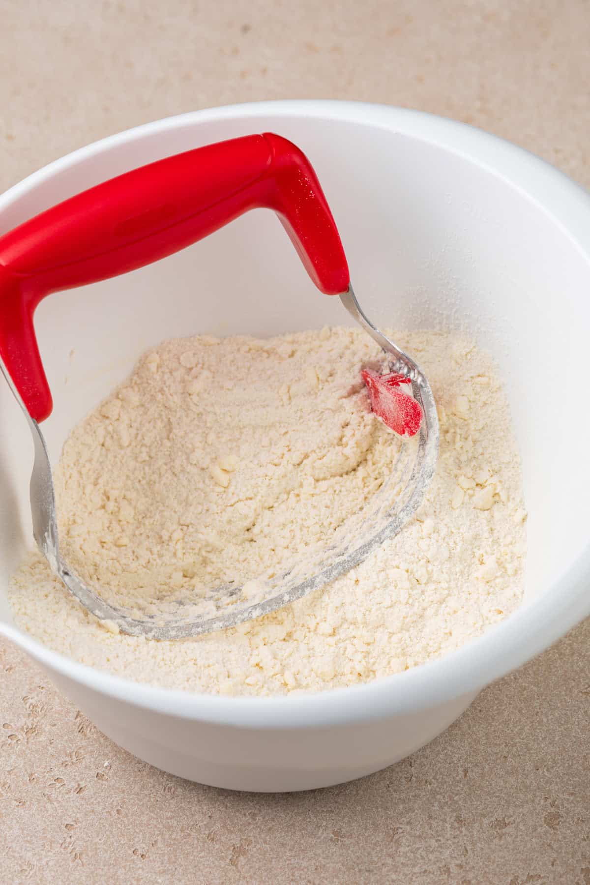 Butter cut into dry ingredients with a pastry blender in a white bowl.