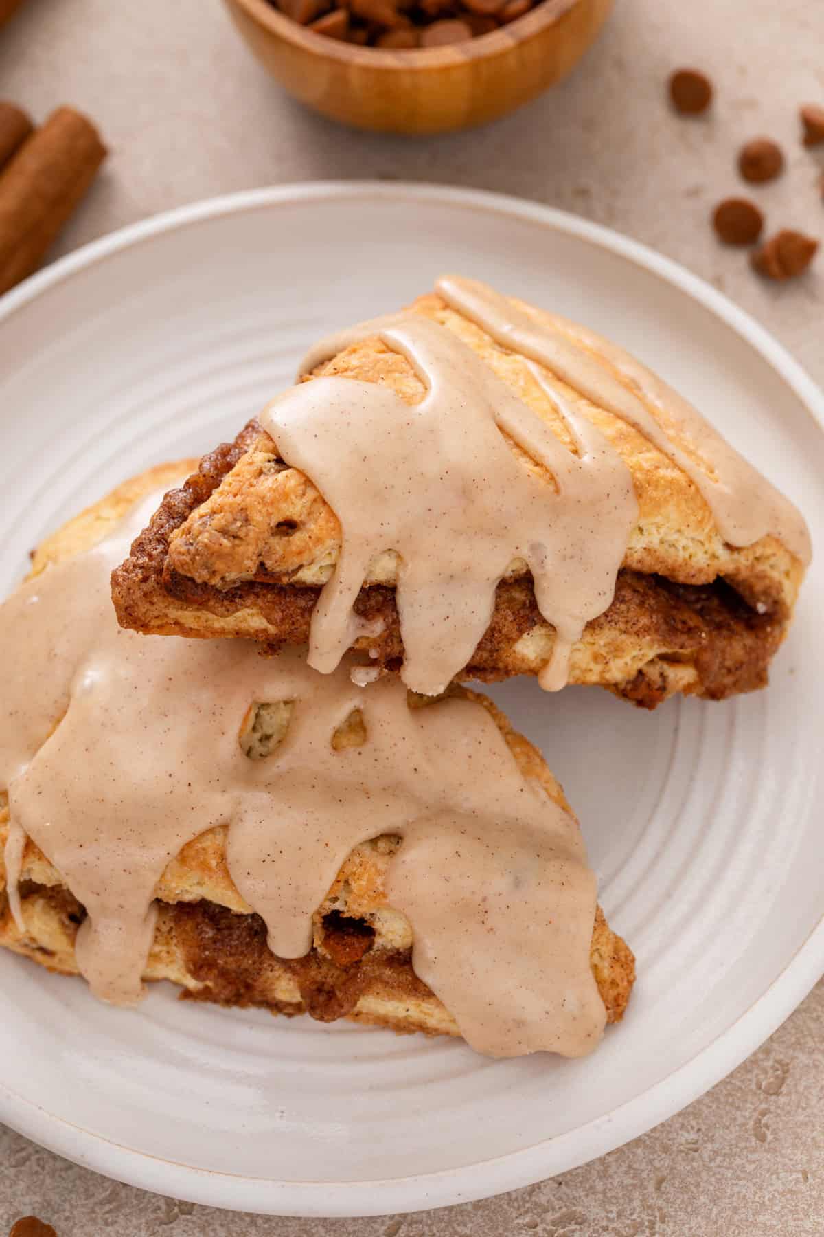 One cinnamon scone leaning against a second on a white plate.