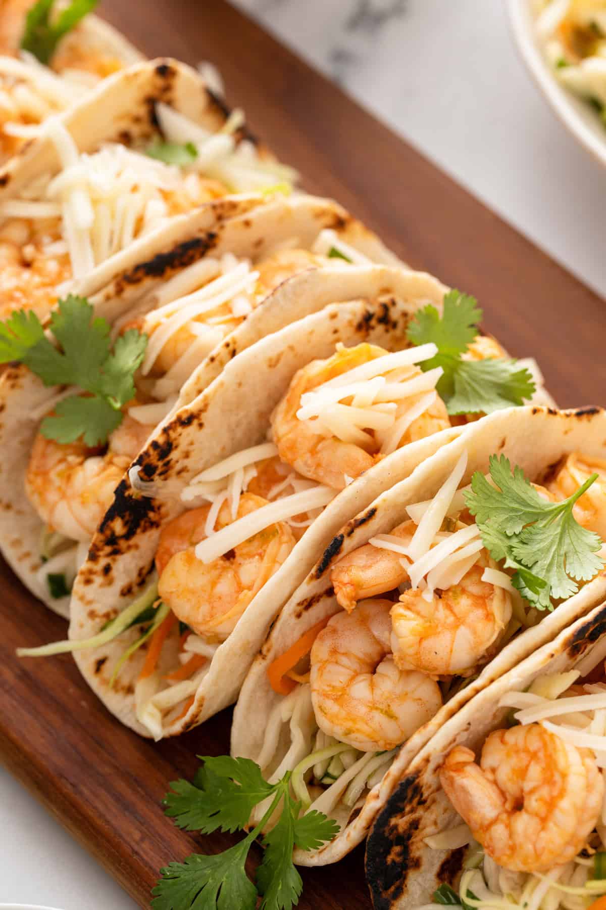 Close up of assembled shrimp tacos on a wooden platter.