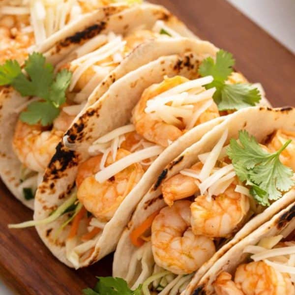 Close up of assembled shrimp tacos on a wooden platter.
