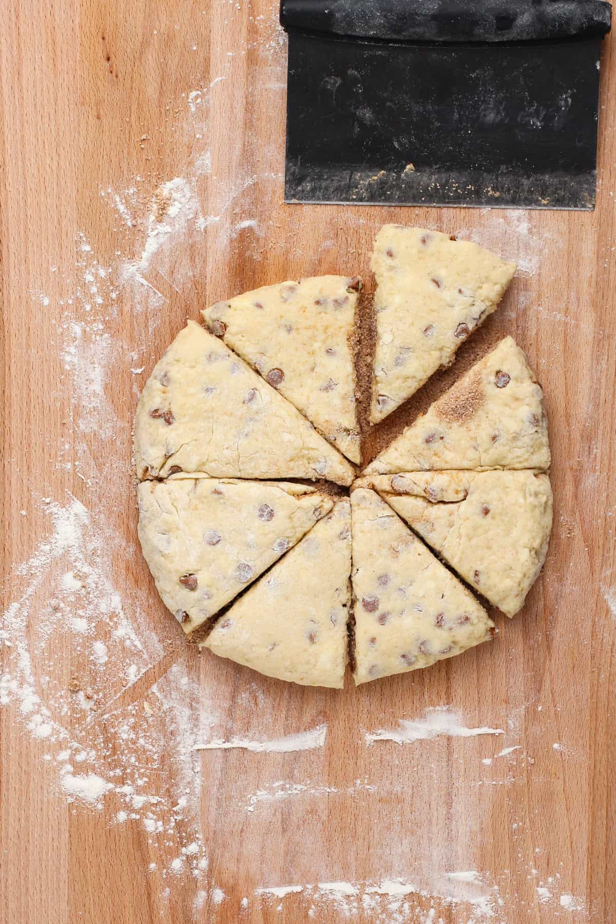 Cinnamon scone dough cut into 8 triangles on a wooden board.