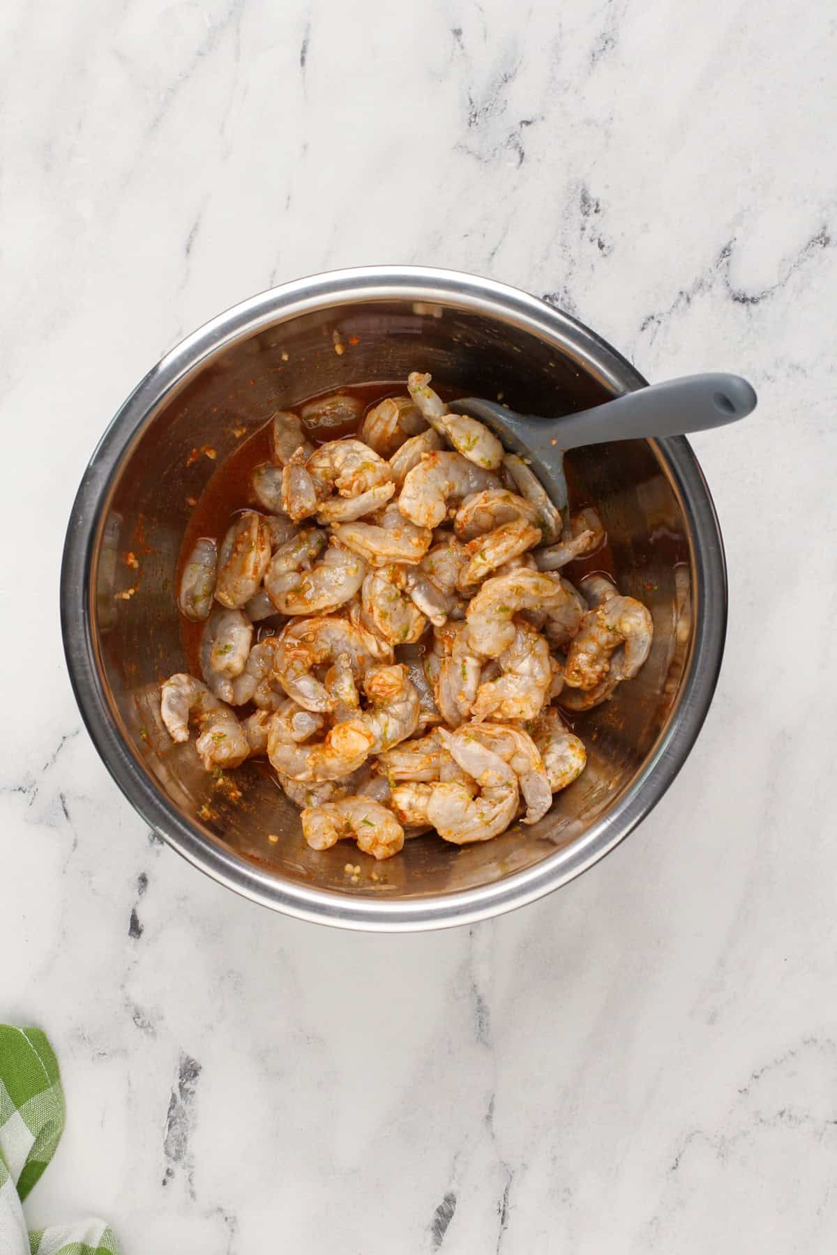 Raw shrimp being mixed with marinade in a metal bowl.