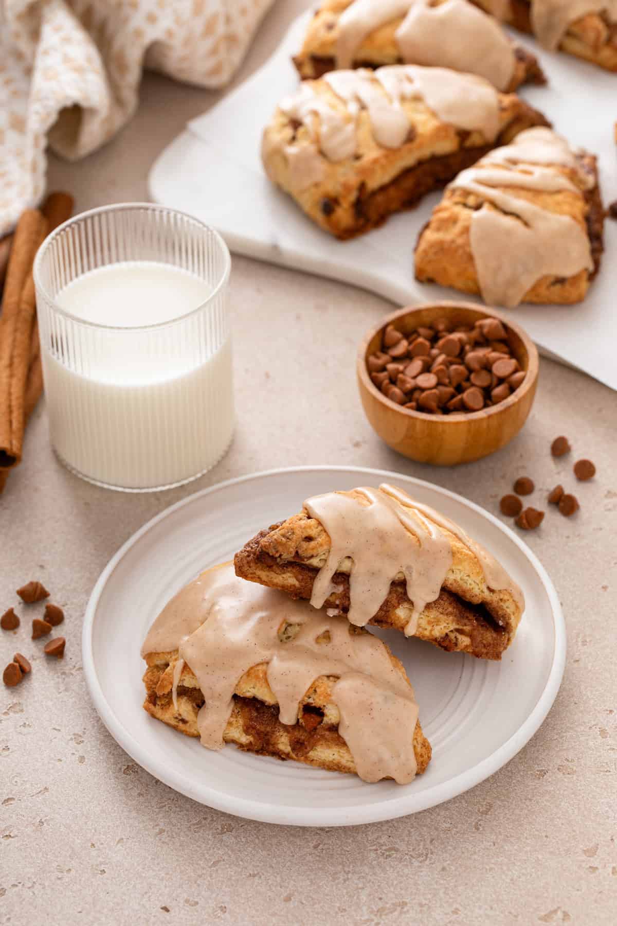 Two cinnamon scones arranged on a white plate in front of a glass of milk.