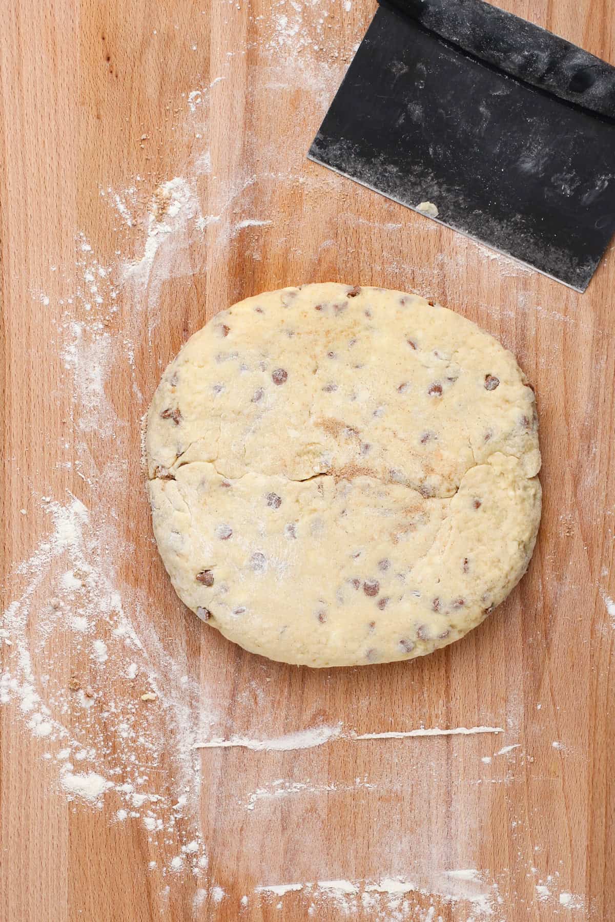 Cinnamon scone dough formed into a circle on a wooden board.