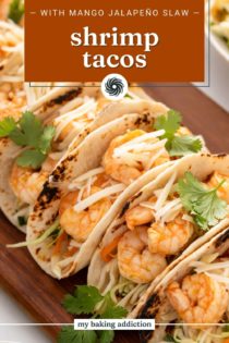 Close up of assembled shrimp tacos on a wooden platter. Text overlay includes recipe name.