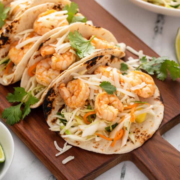 Assembled shrimp tacos with slaw on a wooden platter.