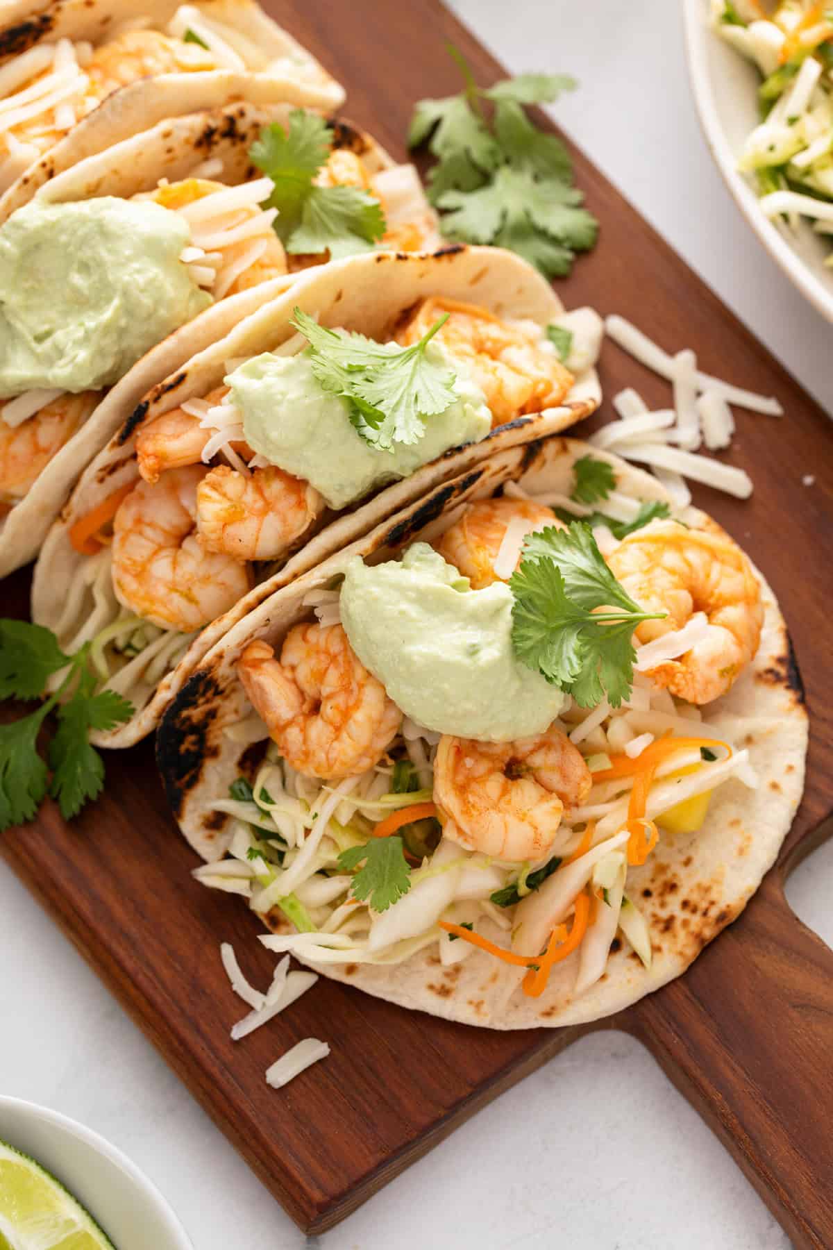 Shrimp tacos assembled and topped with avocado crema on a wooden board.