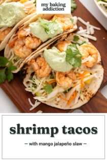 Shrimp tacos assembled and topped with avocado crema on a wooden board. Text overlay includes recipe name.