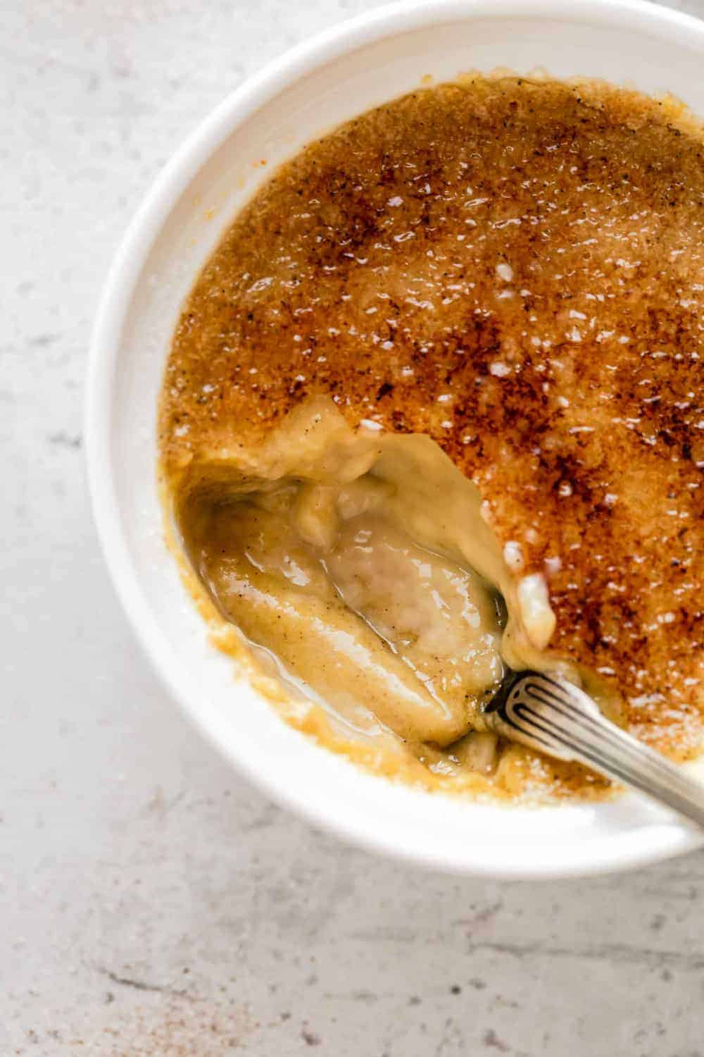 Bite taken out of a pumpkin creme brulee, showing the pumpkin custard underneath the bruleed sugar topping