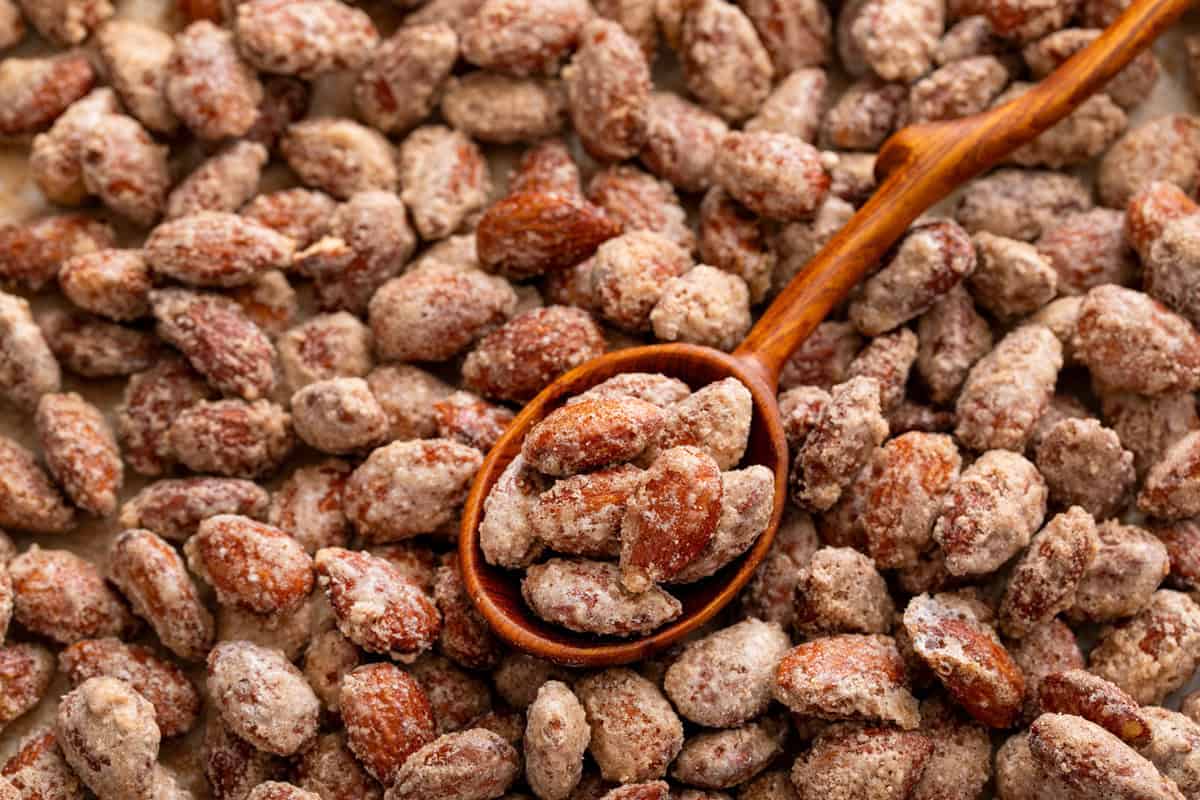 Wooden spoon holding candied almonds set on a bed of candied almonds.