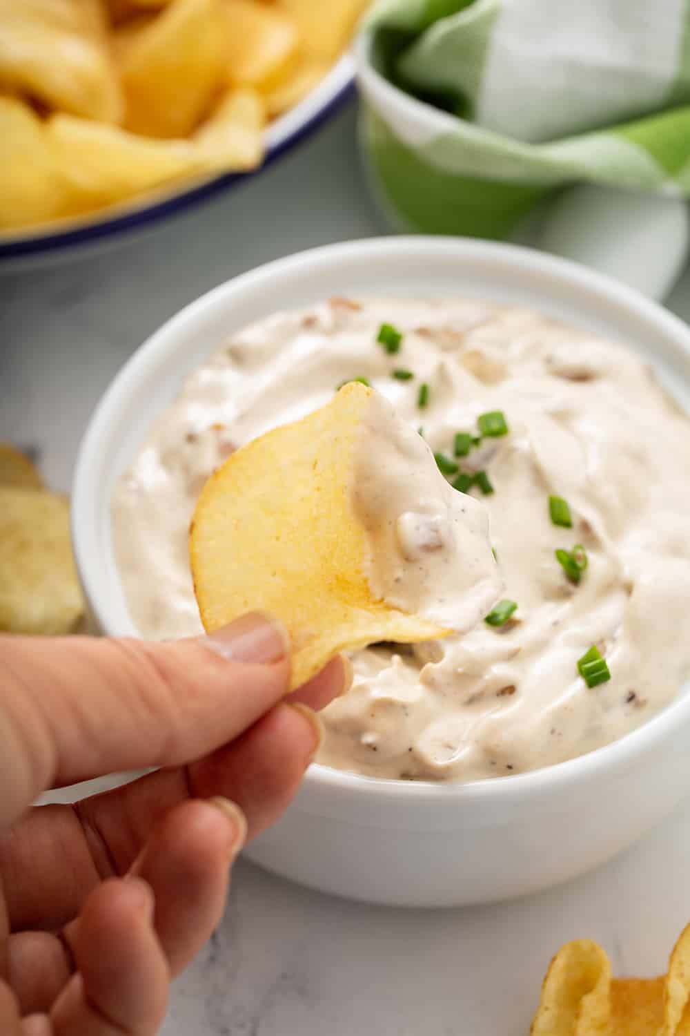 Hand scooping up french onion dip with a potato chip