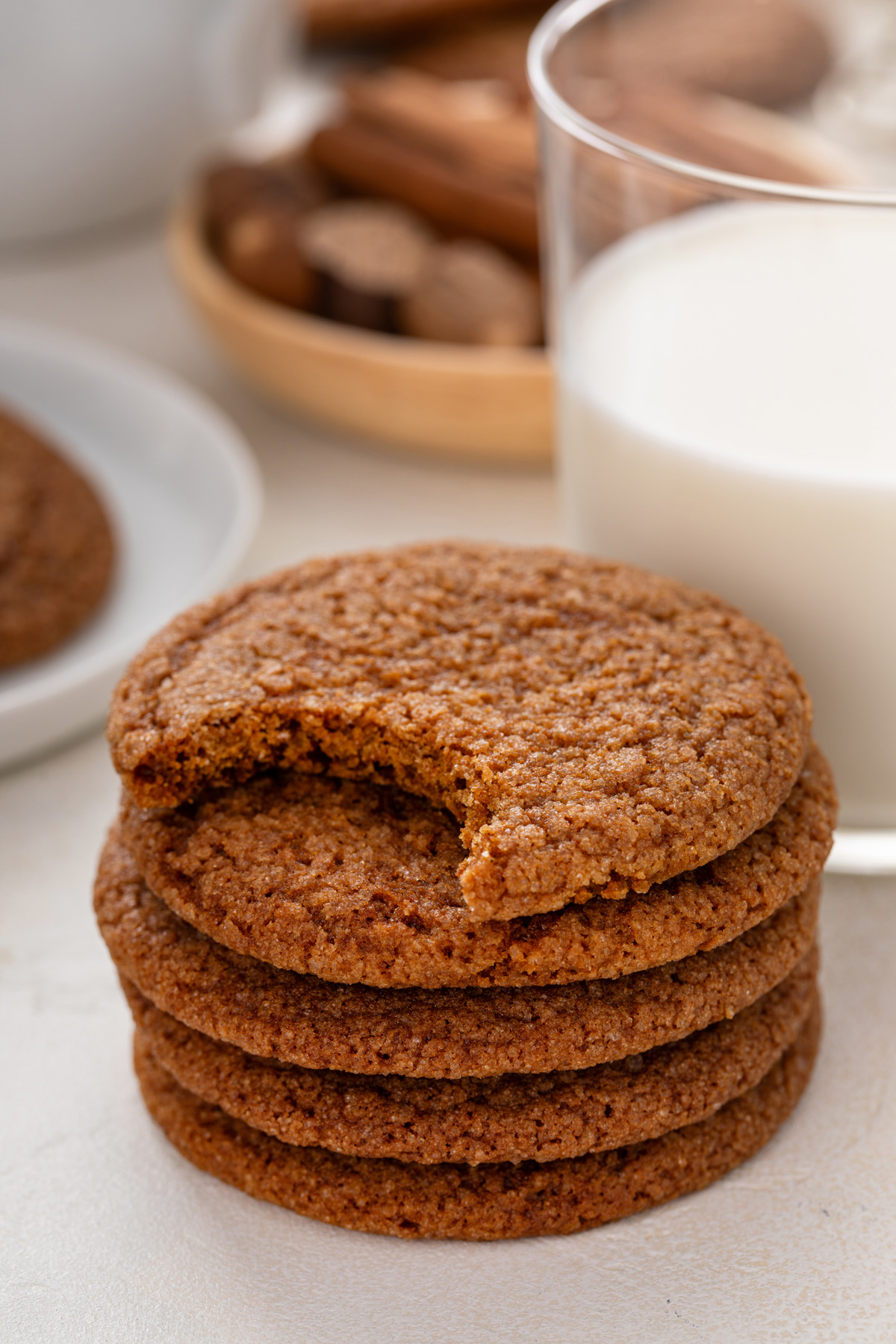 Five molasses cookies stacked next to a glass of milk. The top cookie has a bite taken out of it.