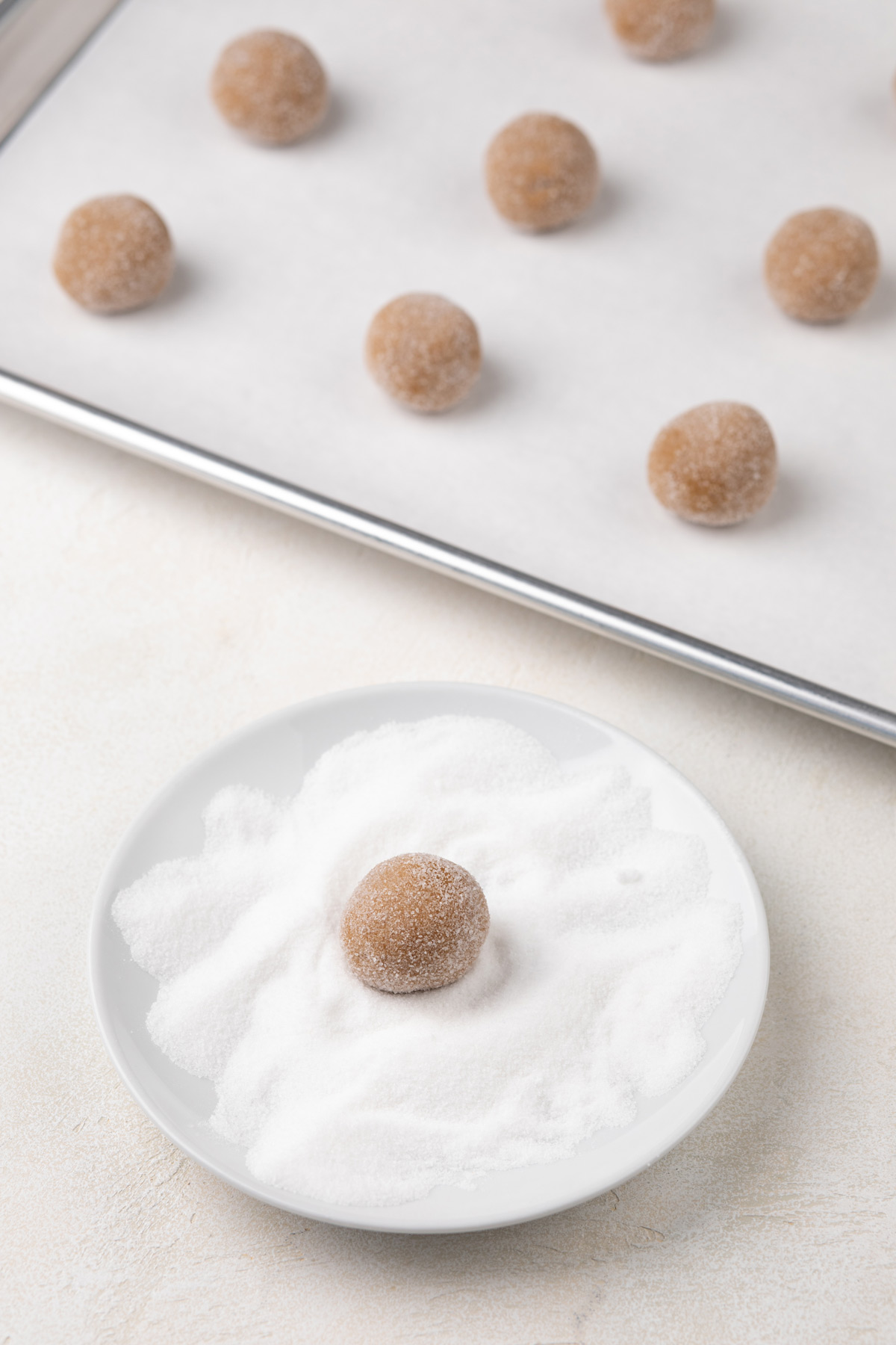 Molasses cookie dough ball being rolled in granulated sugar.