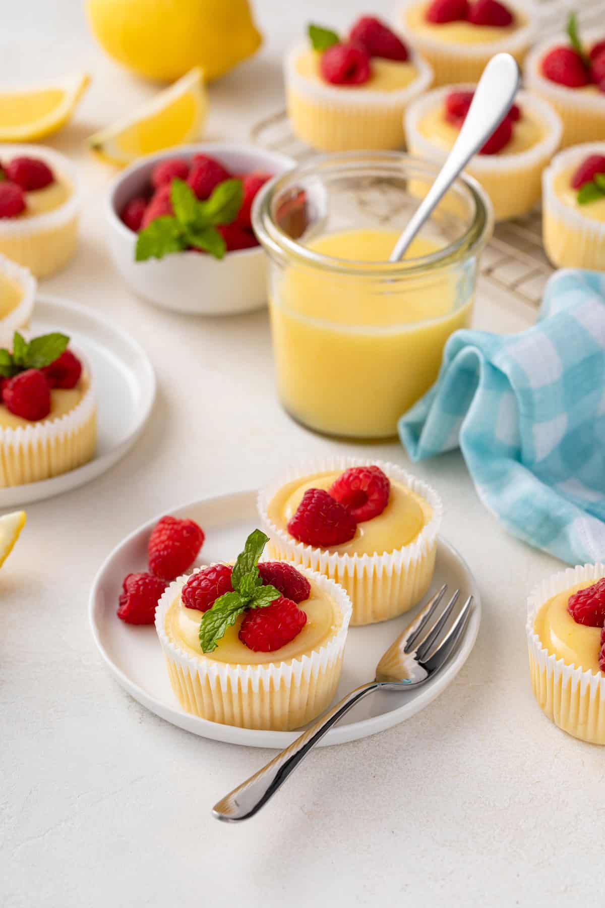 Two mini lemon cheesecakes on a white plate next to a jar of lemon curd.