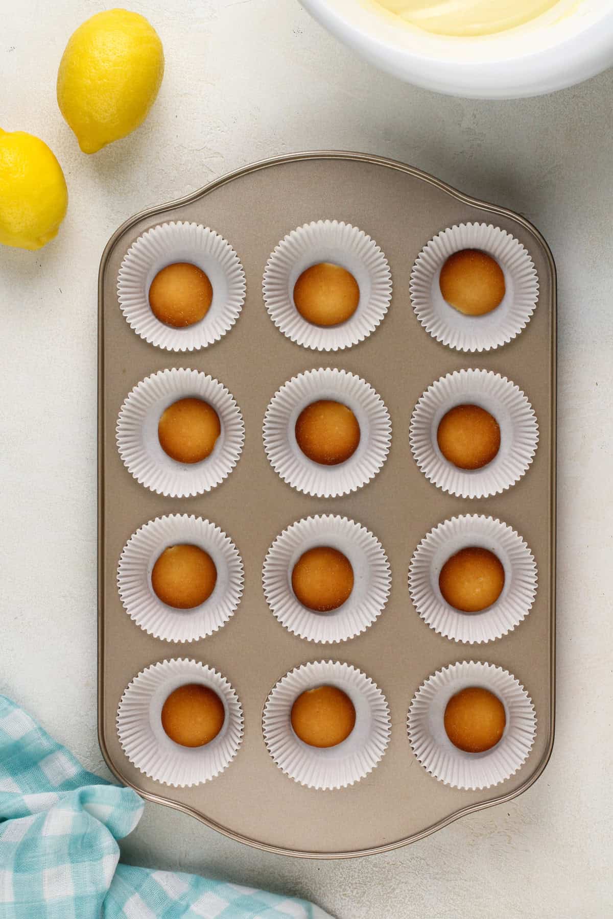 Vanilla wafer cookies in the bottom of muffin cups in a muffin pan.