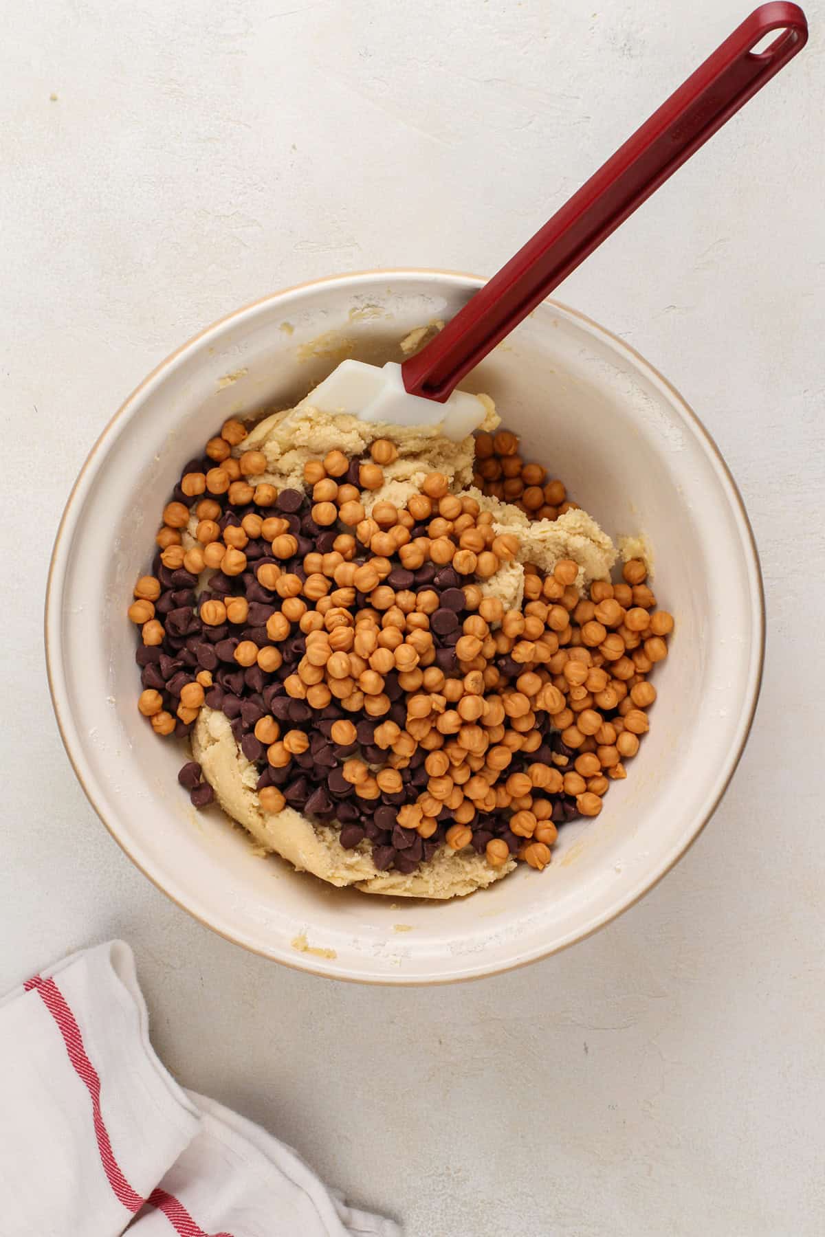Chocolate chips and caramel bits being added to cookie dough in a mixing bowl.