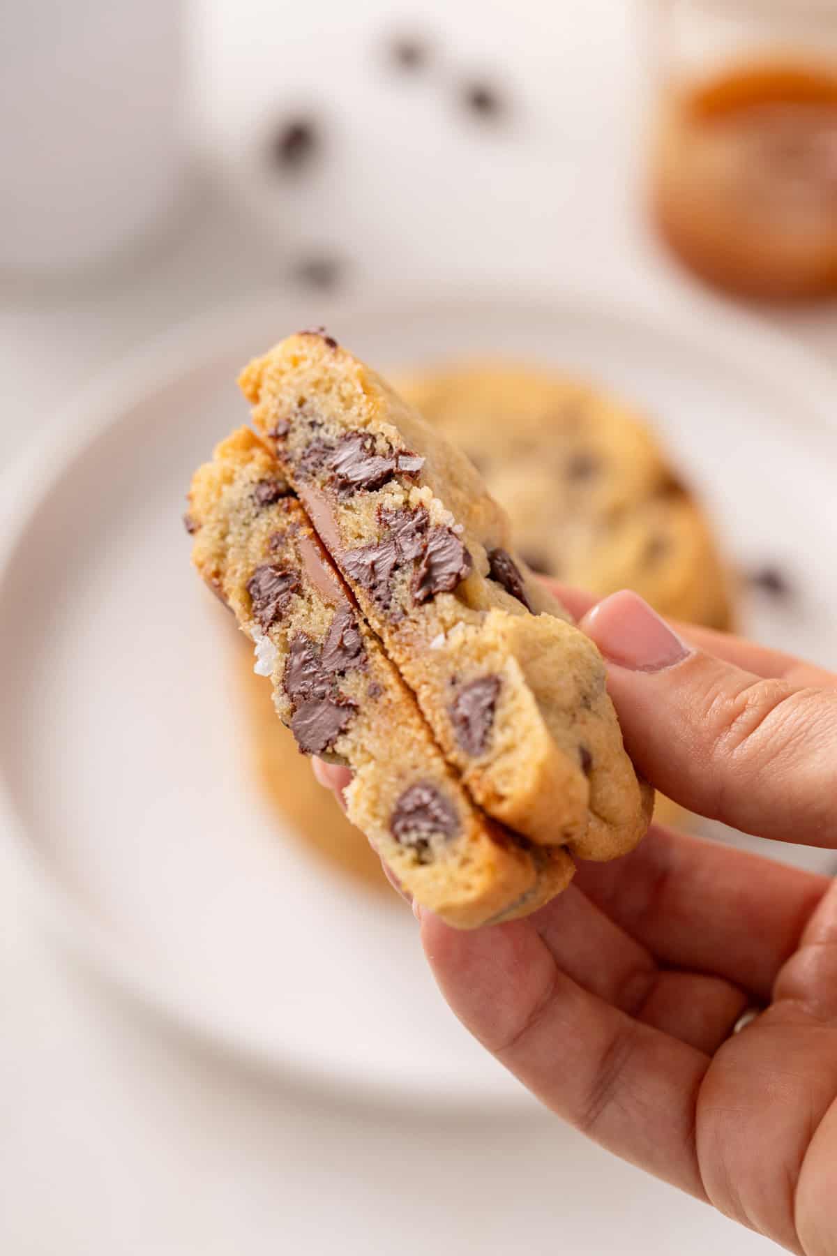 Hand holding up a halved salted caramel chocolate chip cookie.