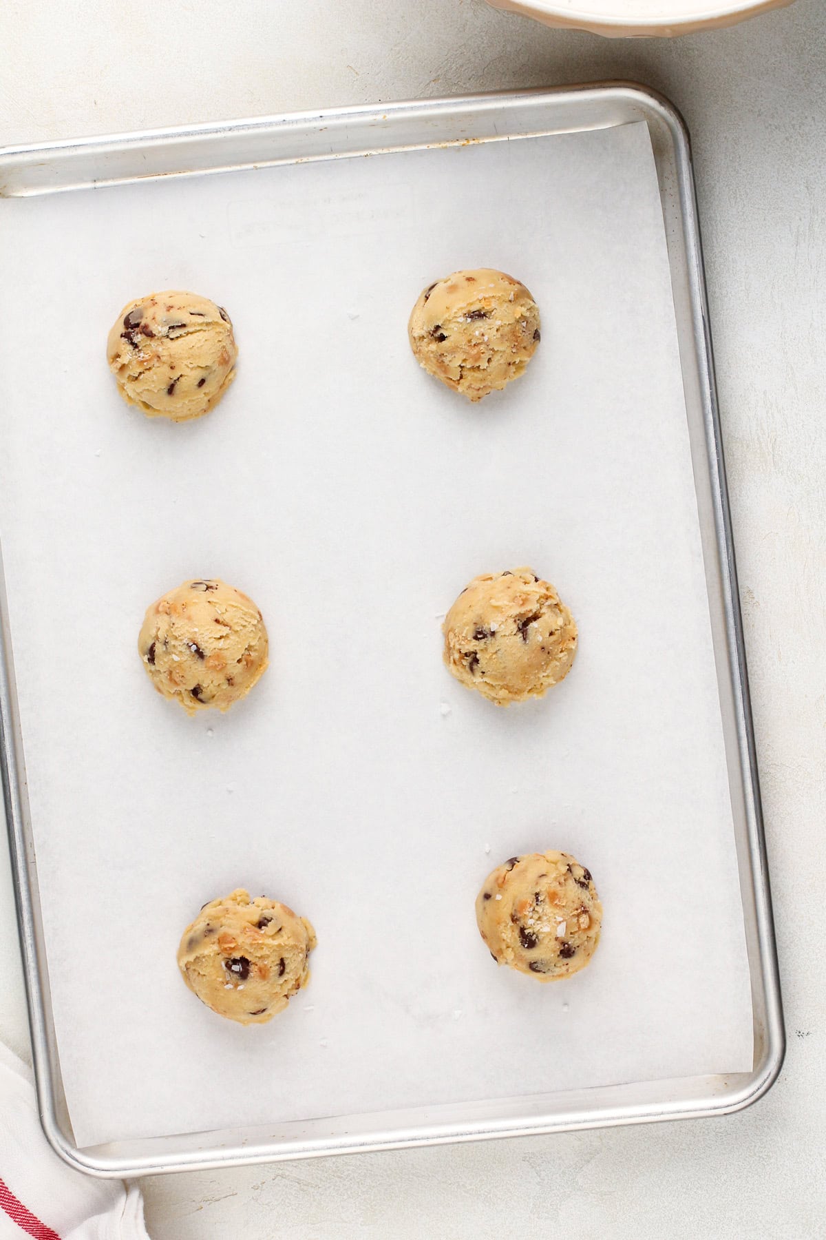 6 balls of salted caramel chocolate chip cookie dough on a lined baking sheet, ready to be baked.