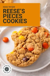 Two reese's pieces cookies on a white plate. The top cookie has a bite taken from it. Text overlay includes recipe name.