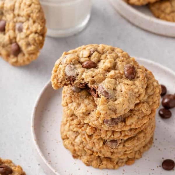 Stack of oatmeal raisin cookies on a white plate. The top cookie has a bite taken out of it.