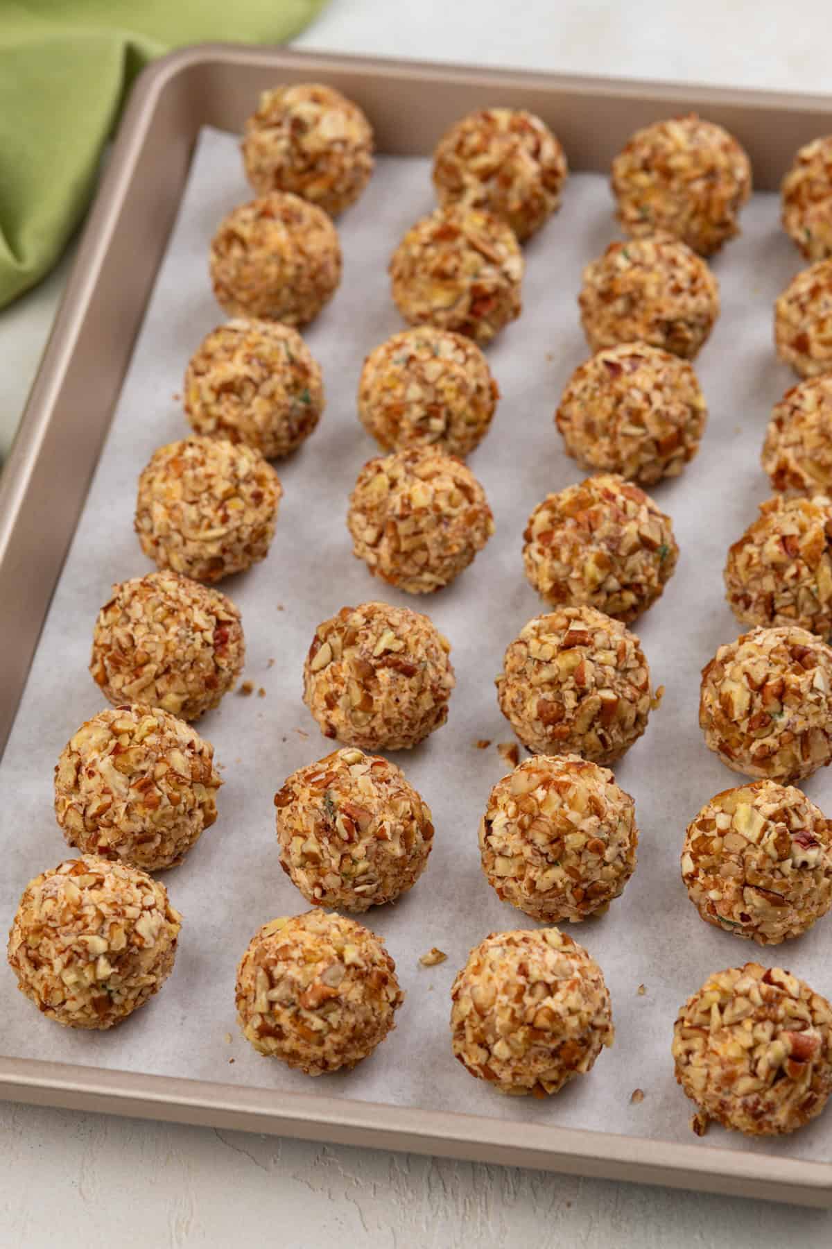 Mini cheese balls rolled in pecans and lined up on a sheet tray.