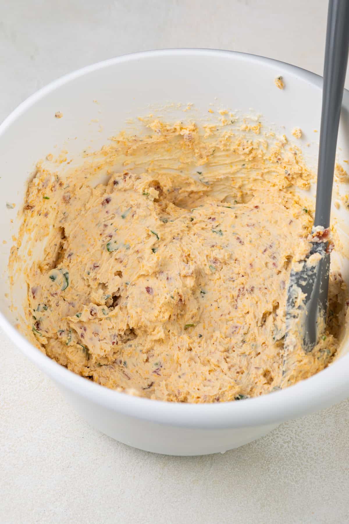 Mixture for mini cheese balls in a white mixing bowl.