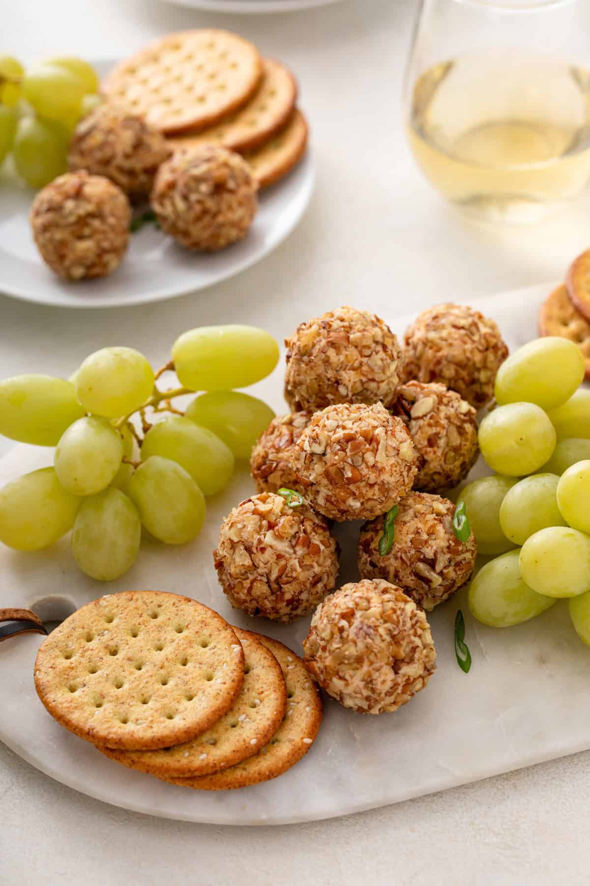 Mini cheese balls next to grapes and crackers on a marble board.