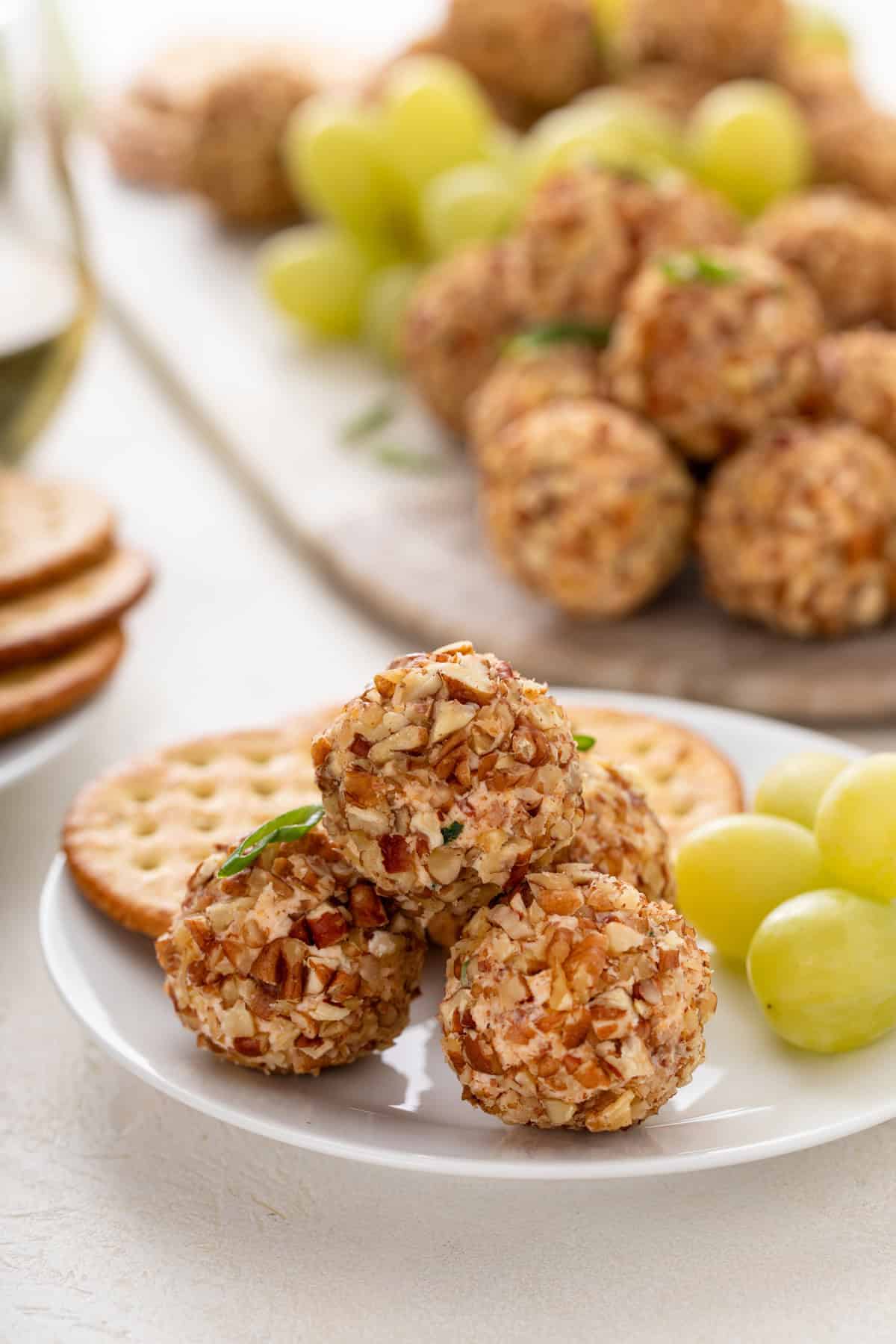 Several mini cheese balls next to grapes and crackers on a white plate.