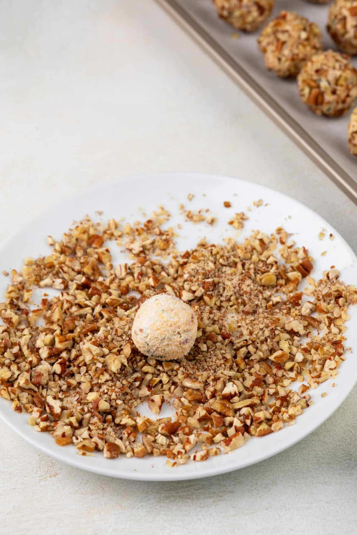 Mini cheese ball being rolled in chopped pecans.