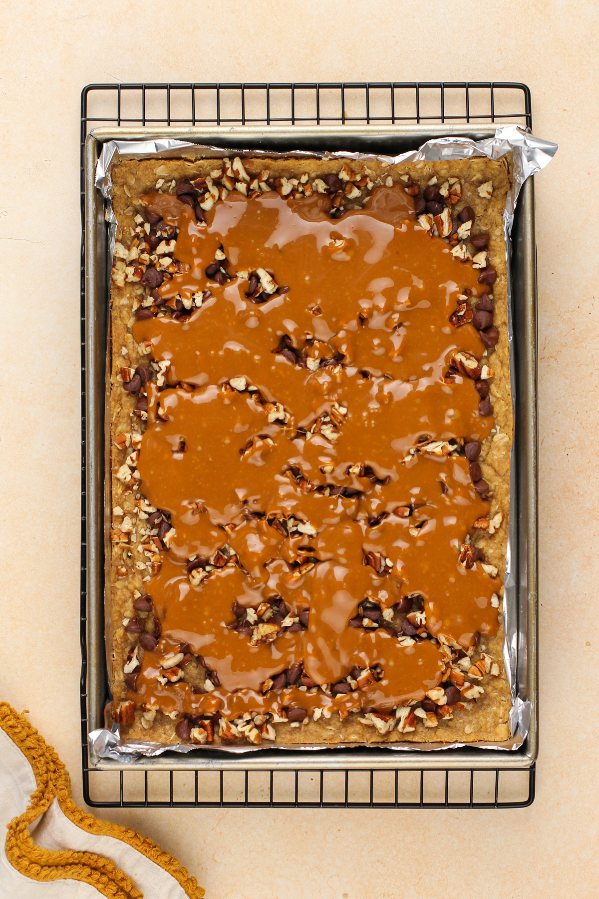 Pecans, chocolate chips, and melted caramel on top of a crust for caramel pecan bars.