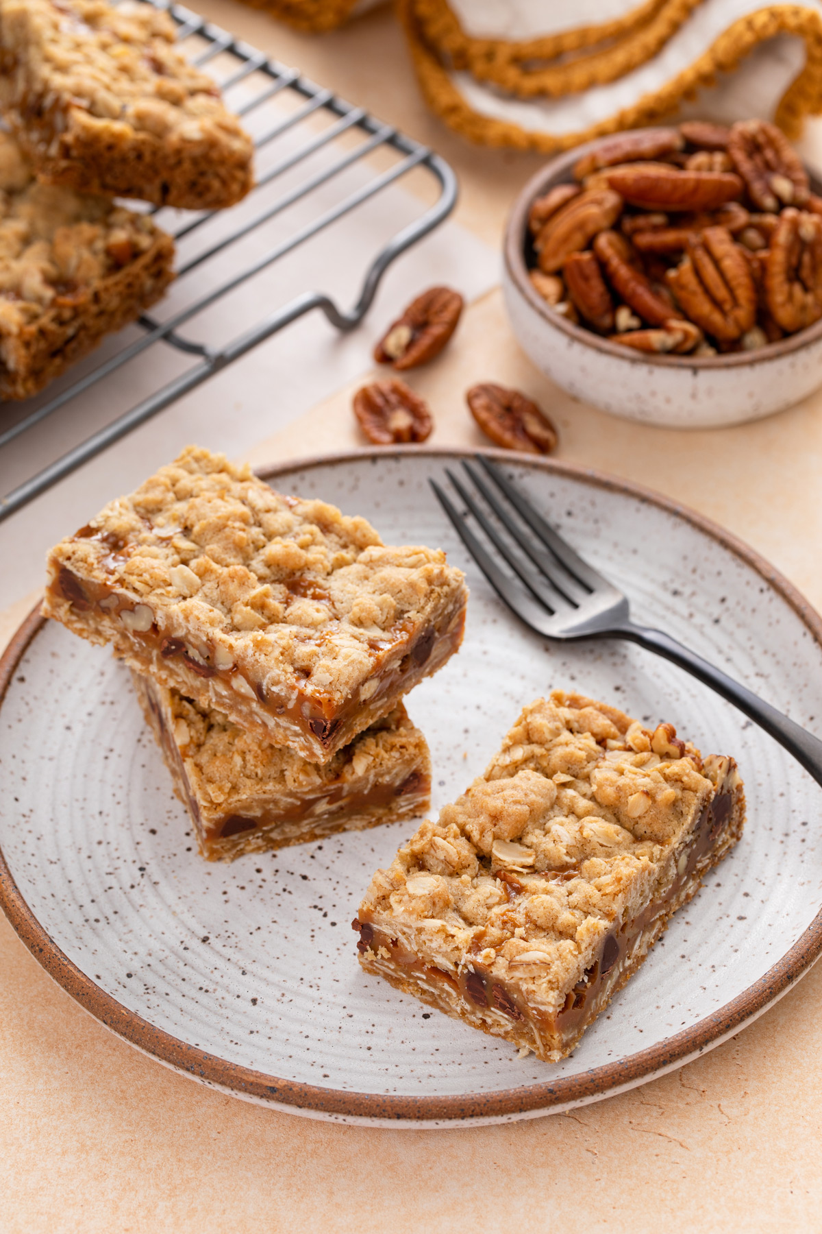 Three caramel pecan bars next to a fork on a plate.