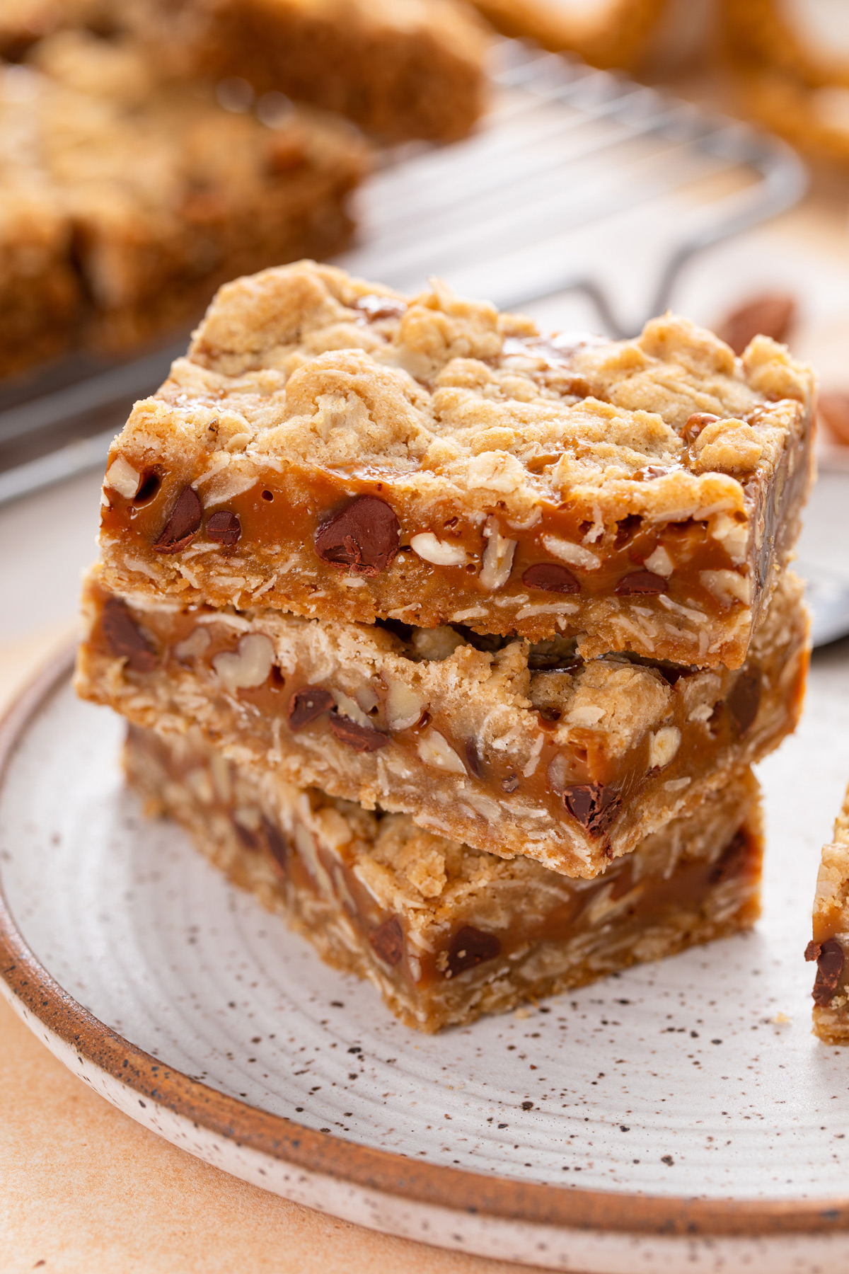 Three caramel pecan bars stacked on a plate.