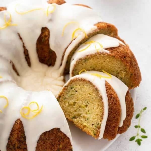 Sliced lemon zucchini bundt cake on a white cake plate.