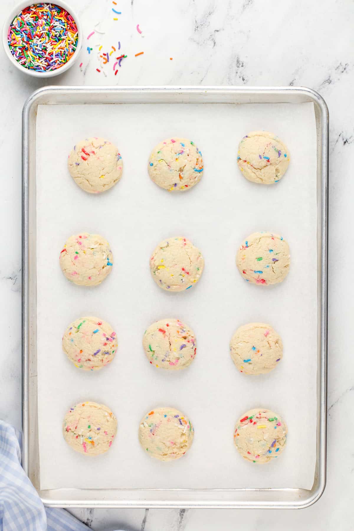 Baked birthday cake cookies on a lined baking sheet.
