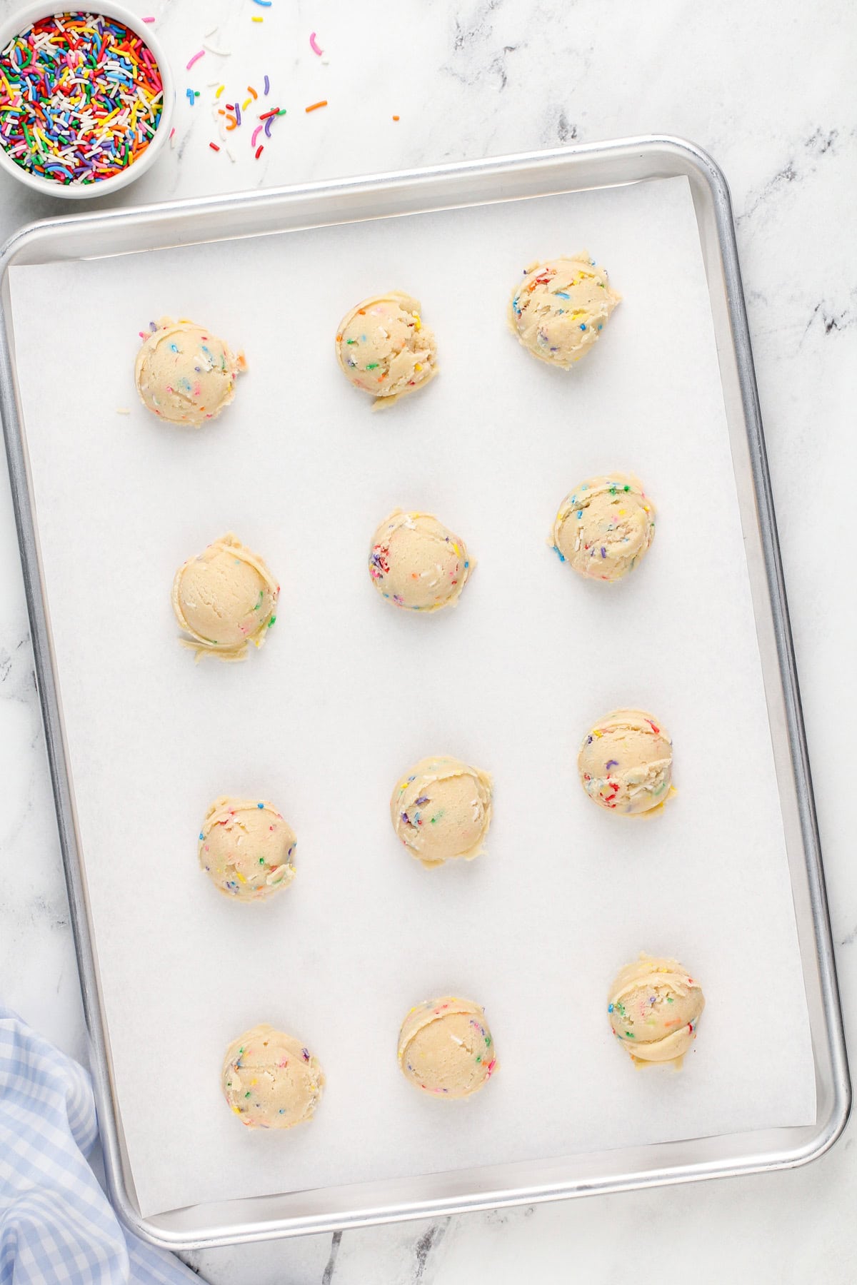 Portioned birthday cake cookie dough on a lined baking sheet, ready to go in the oven.