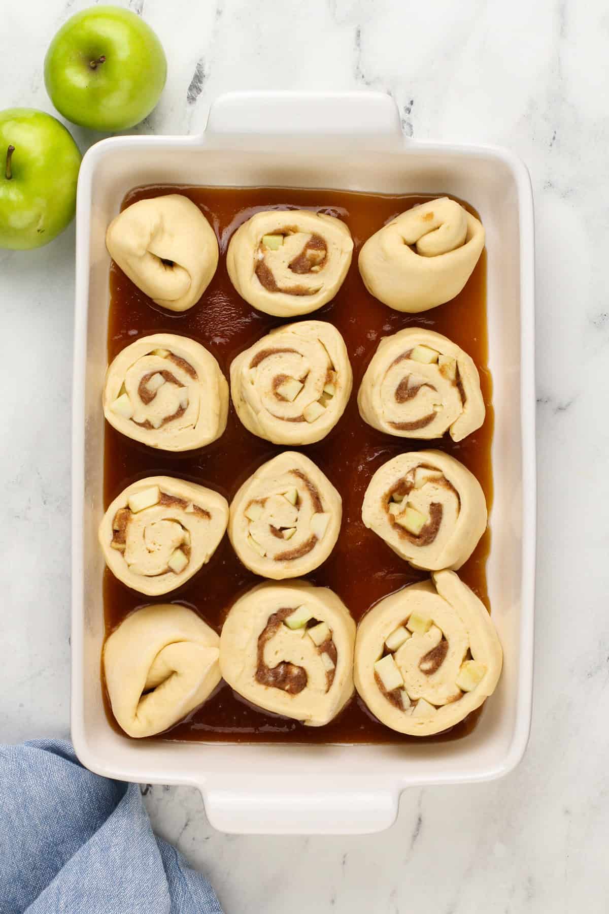 Caramel apple cinnamon roll pieces set on top of caramel sauce in baking dishes.