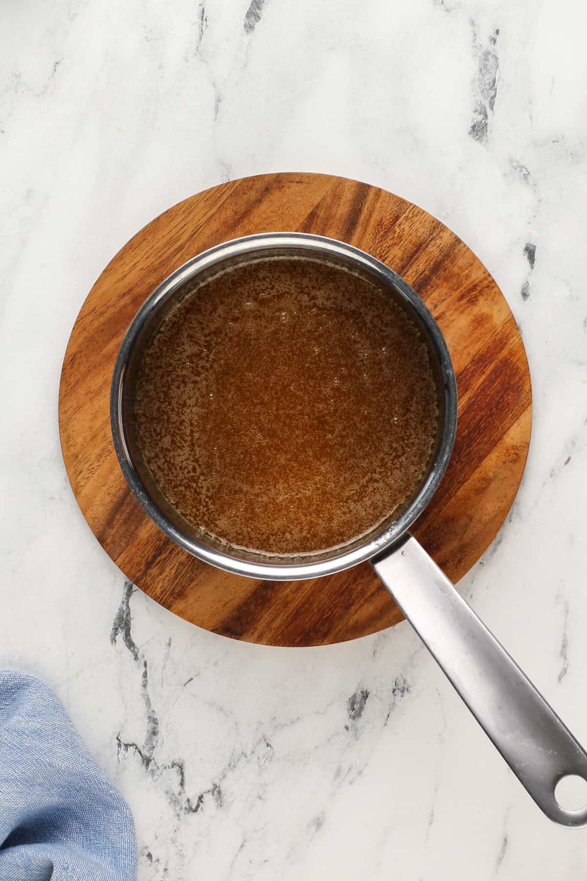 Caramel sauce in a saucepan on a wooden trivet.