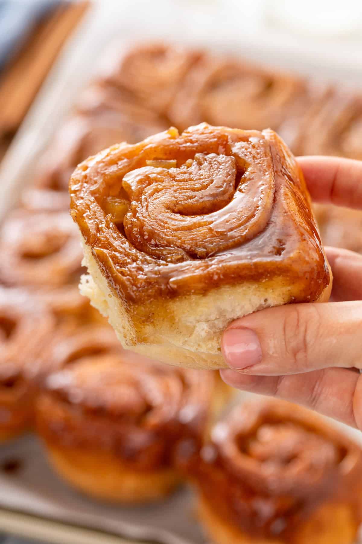 Hand holding up a caramel apple cinnamon roll.