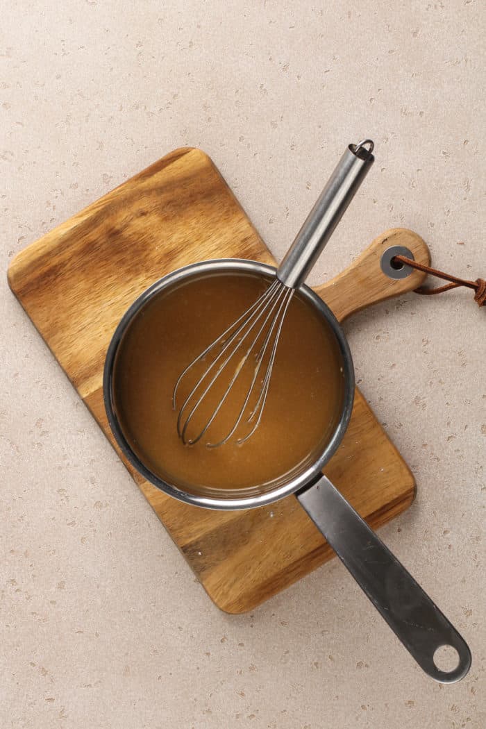 Salted caramel frosting being whisked in a small saucepan set on a wooden trivet.