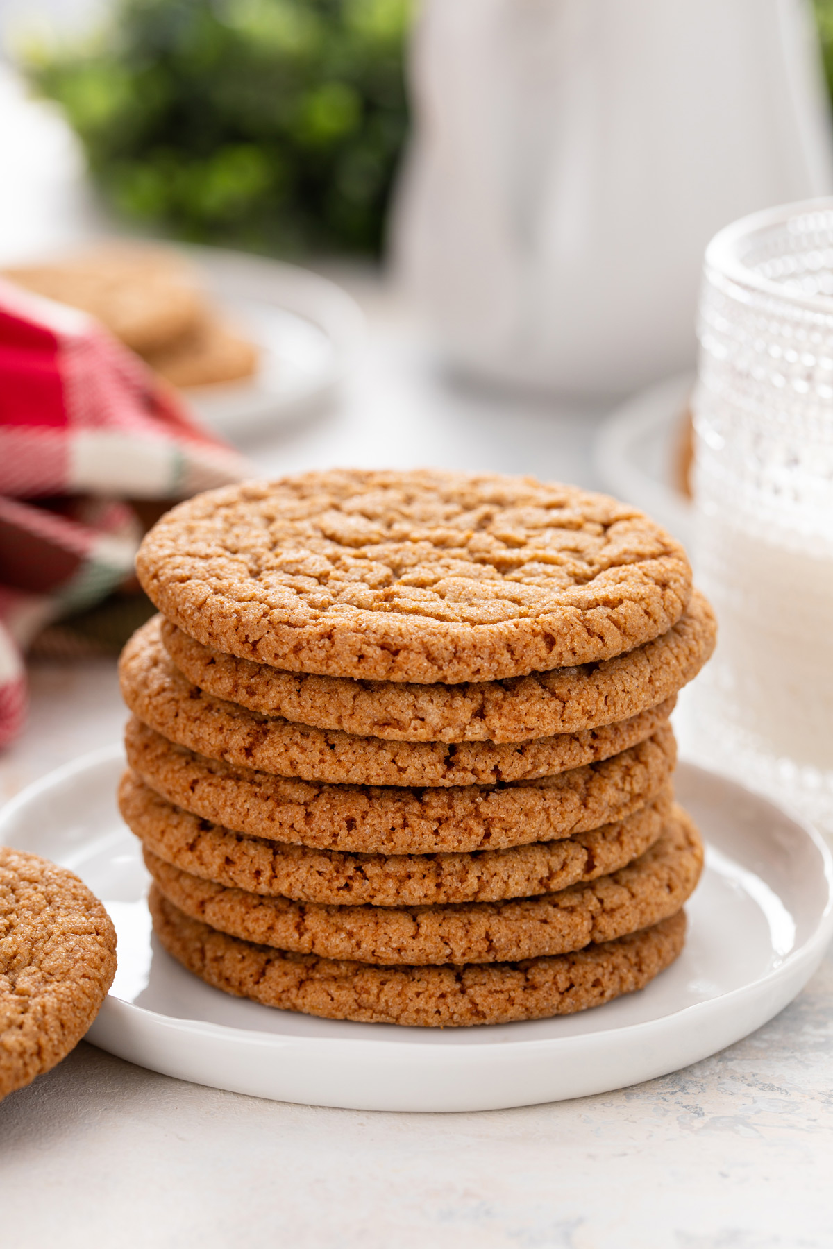 7 gingersnap cookies stacked on a white plate in front of a glass of milk.