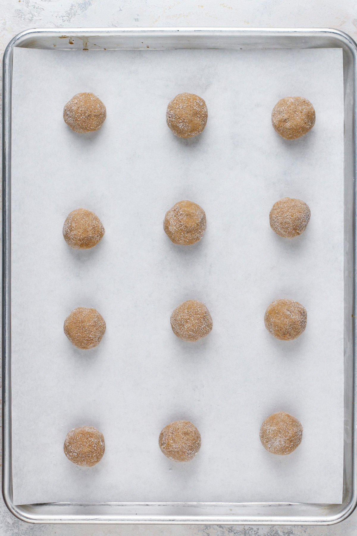 Balls of gingersnap cookie dough arranged on a parchment-lined baking sheet.