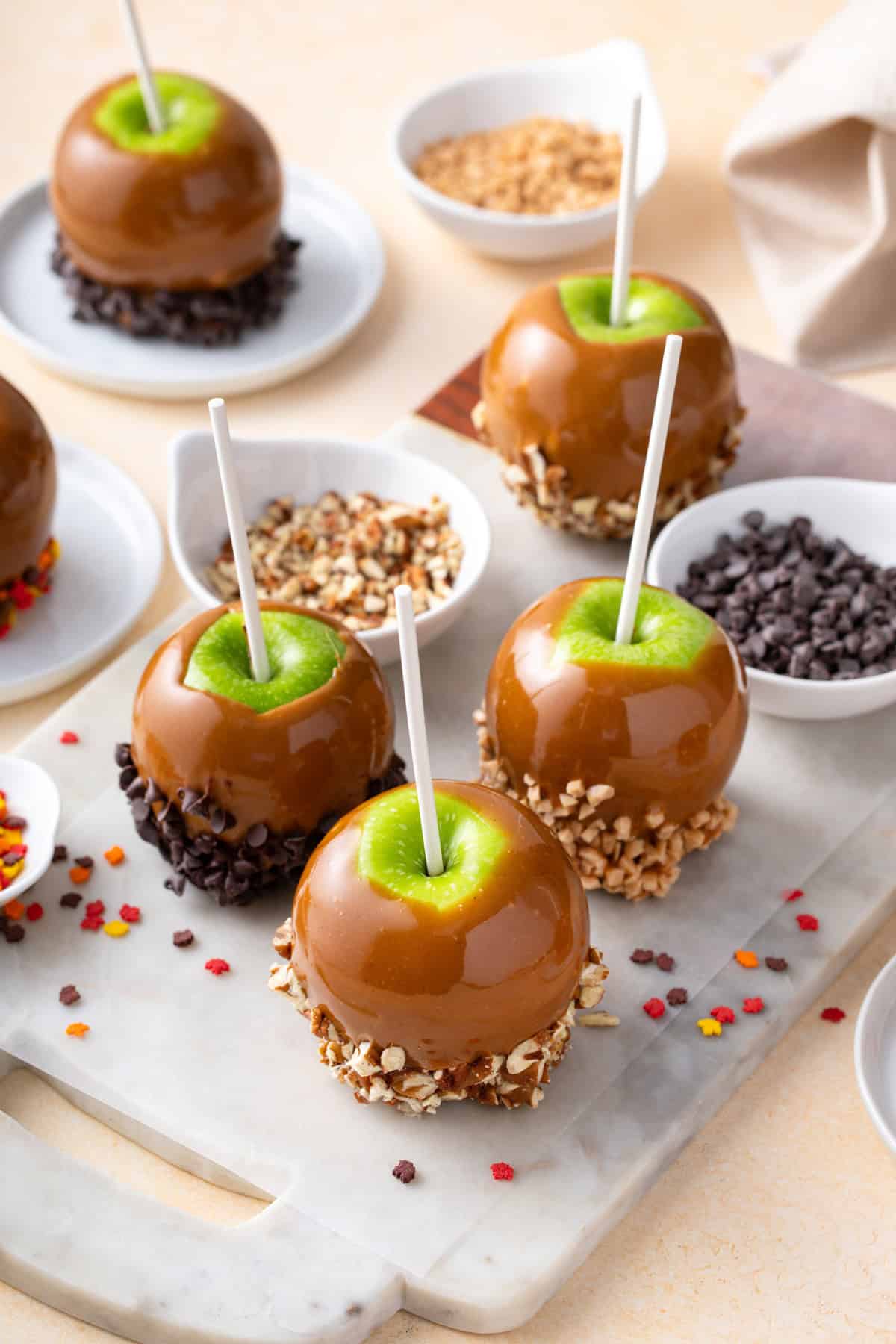 Caramel apples and bowls of assorted topping arranged on a countertop.