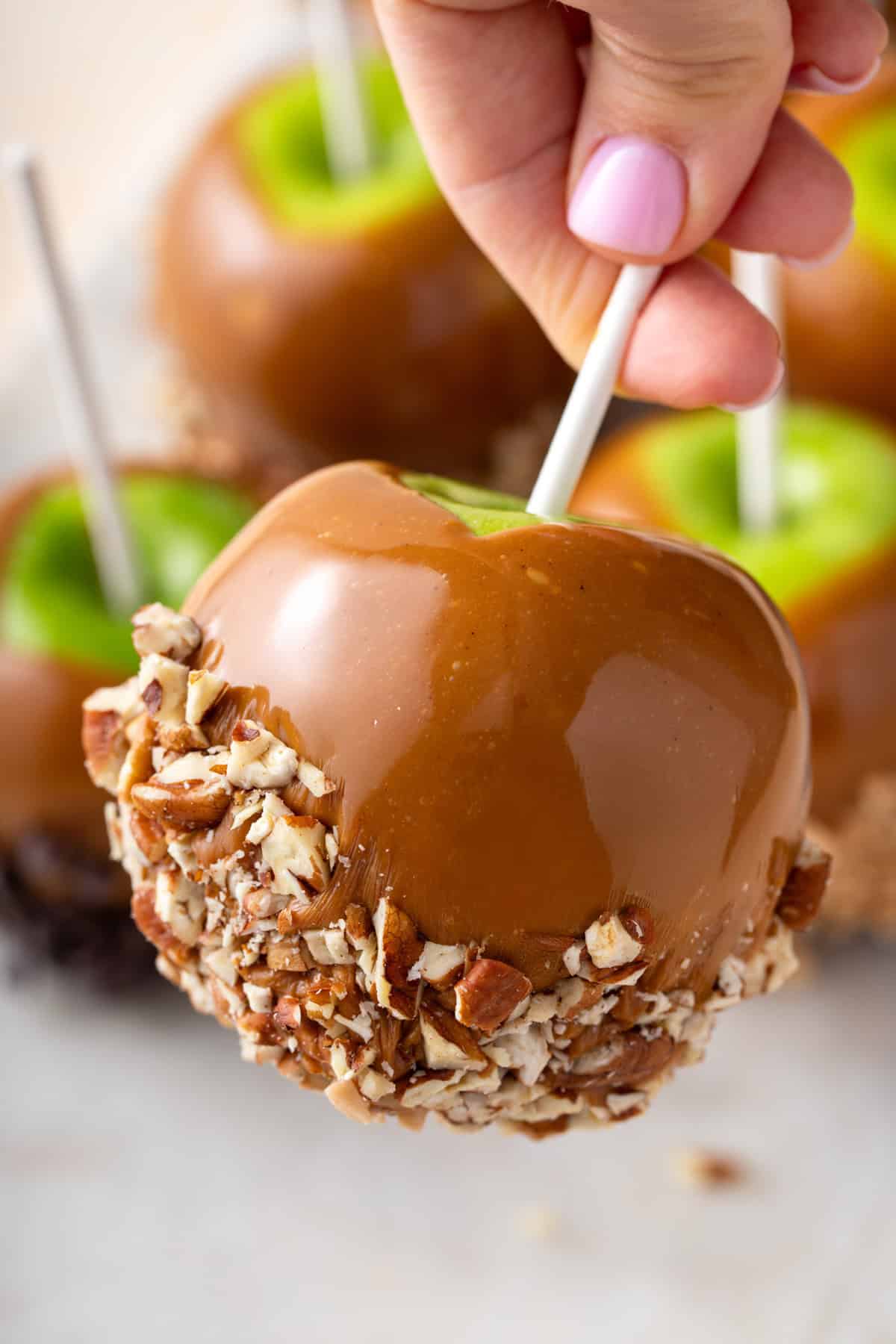 Hand holding up a caramel apple dipped in chopped pecans.