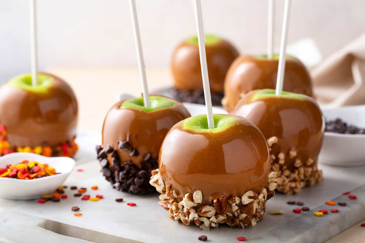 Caramel apples dipped in a variety of toppings on a marble board.