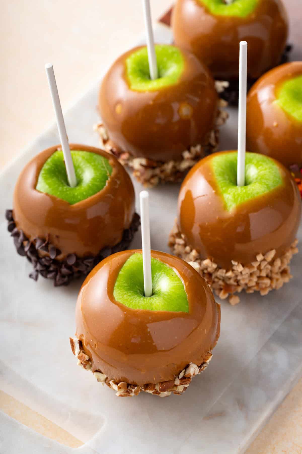 Caramel apples dipped into an assortment of toppings and set on a marble board.