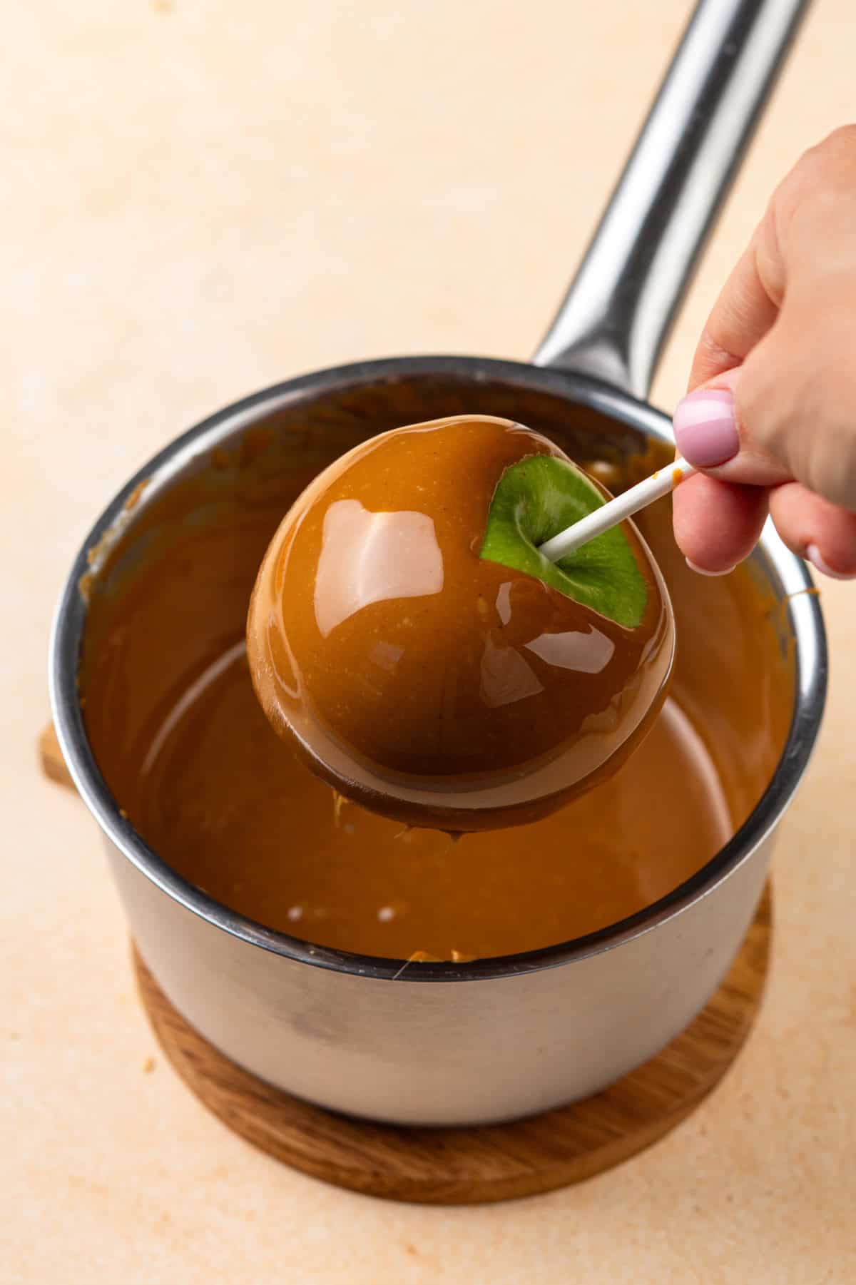 Apple dipped in caramel held over a pot of caramel.