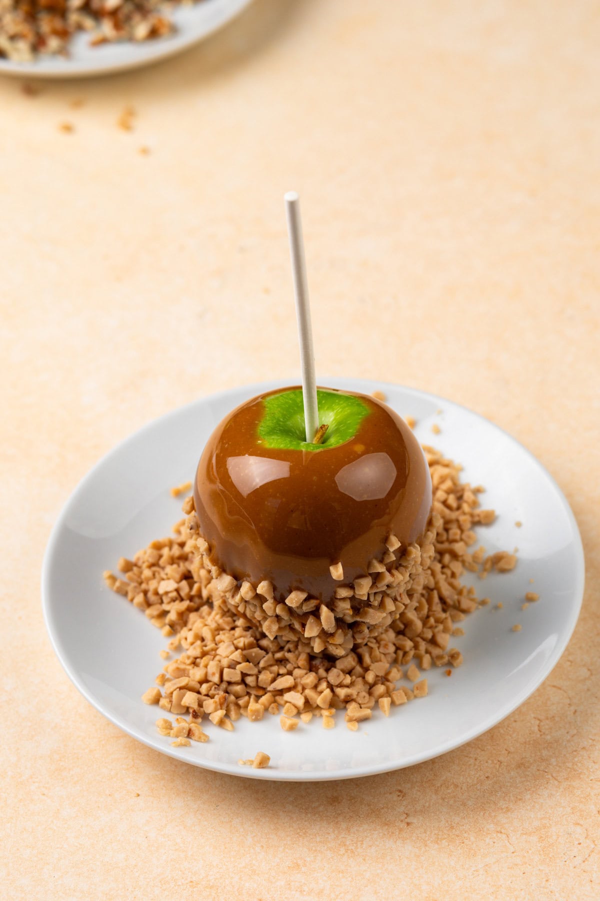 Caramel apple being dipped into chopped nuts.