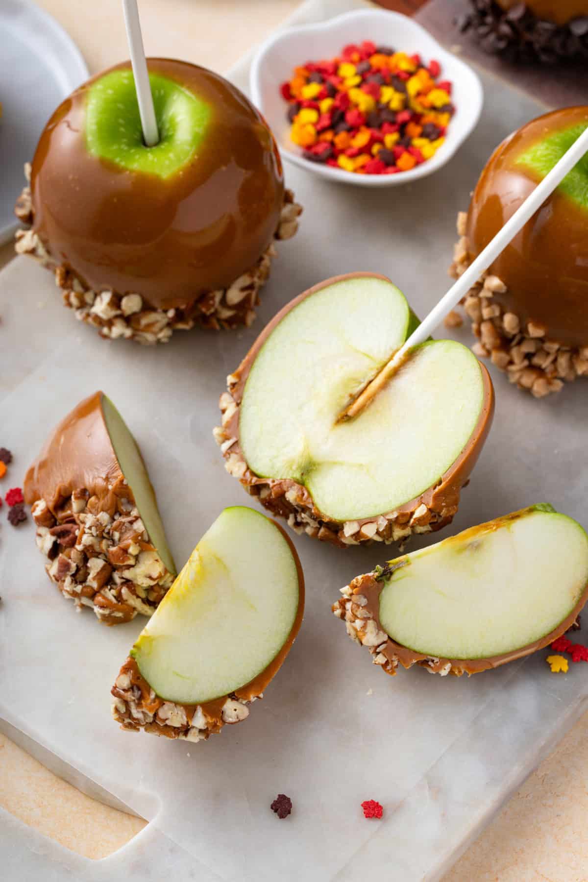 Caramel apple sliced in half and into slices on a marble board.